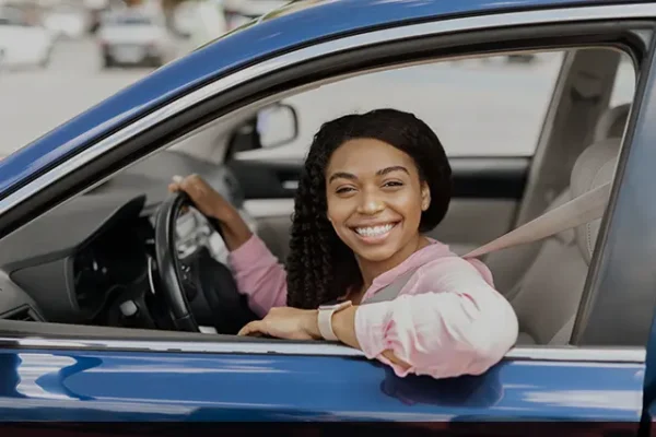 Mulher negra sorrindo no seu carro sabendo que tem seguros para mulheres